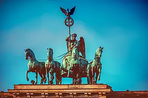 Quadriga mit vier Pferden und einer geflügelten Siegesgöttin auf dem Brandenburger Tor vor blauem Himmel.